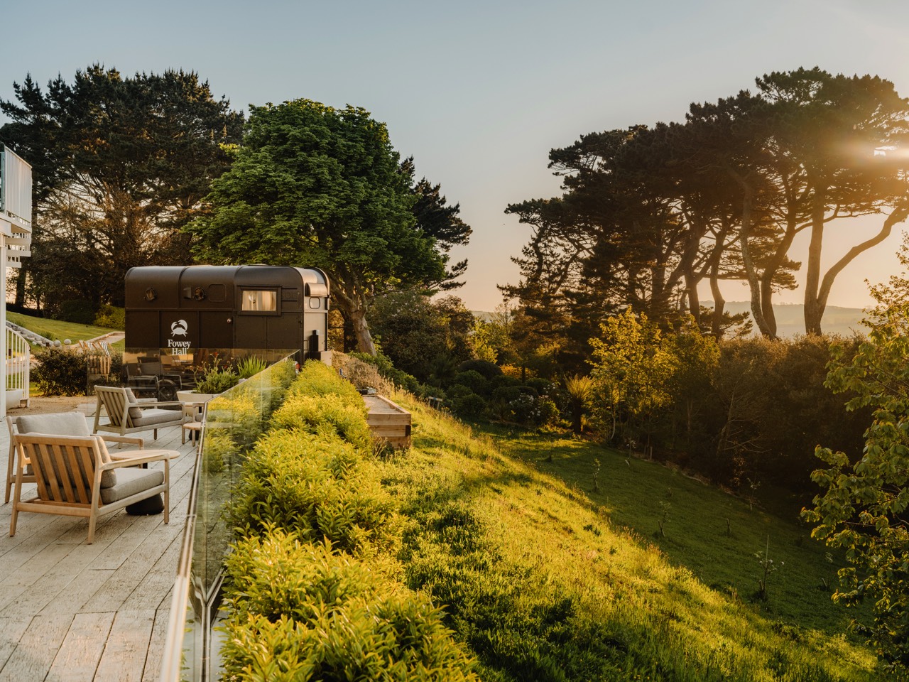 Sauna Box horsebox sauna on the terrace at Fowey Hall Hotel, Cornwall, with lounge chairs and a golden-hour sea view