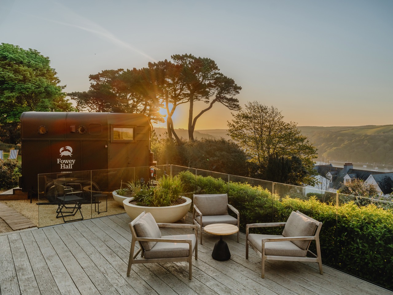 The Fowey Hall sauna on its terrace at sunset, sunlight flaring through pine trees over the valley
