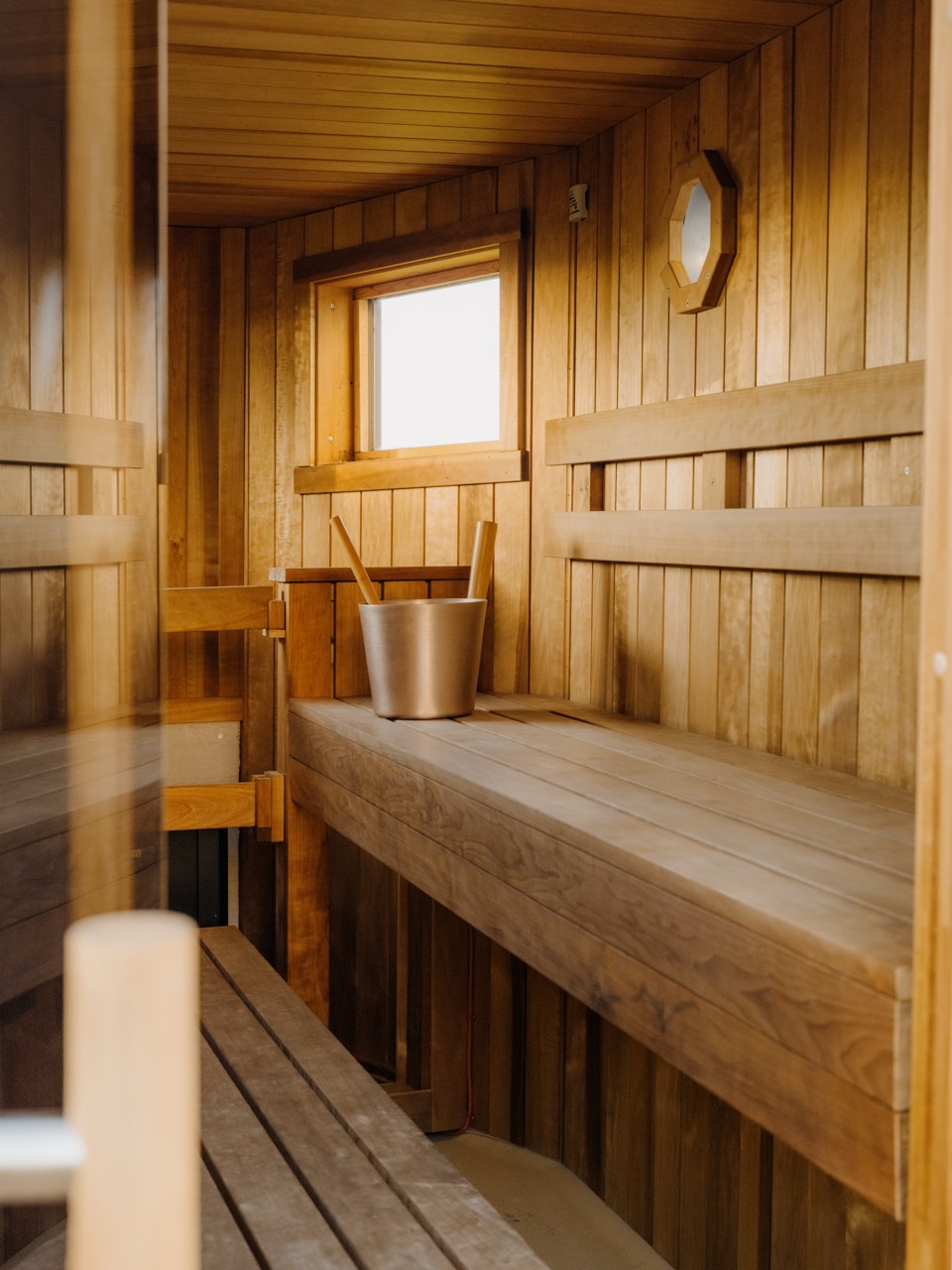 Interior of the Fowey Hall sauna: thermo-timber benches, a window and a traditional bucket and ladle