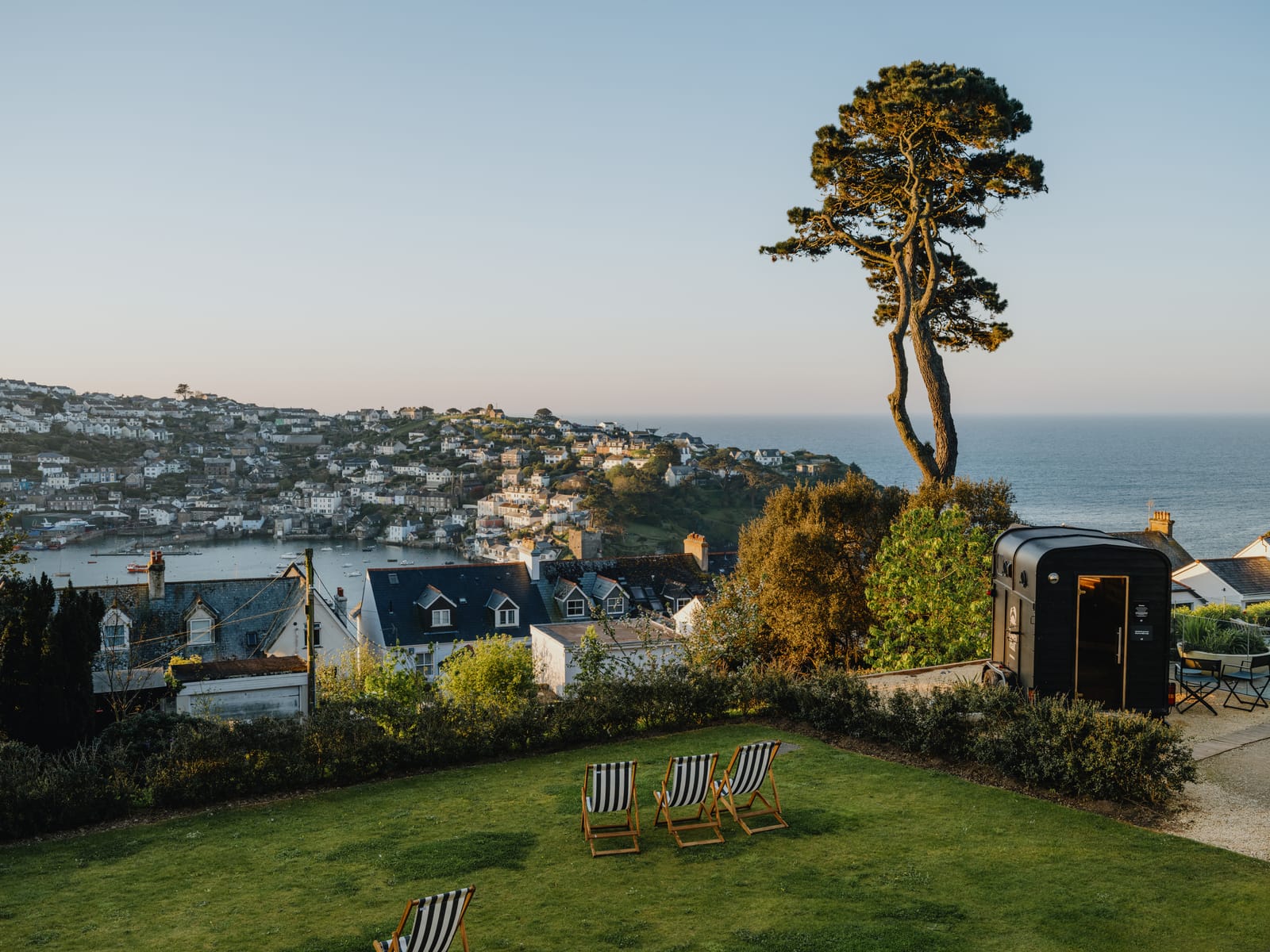 Wide view across the hotel lawn and deckchairs to Fowey town, the lone pine and the open sea