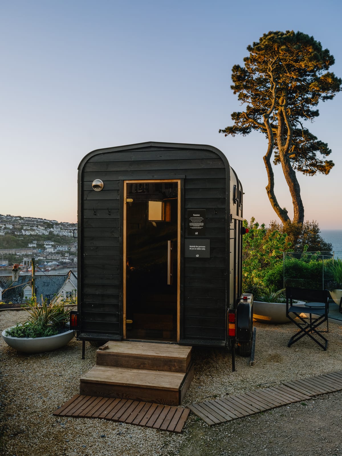 The horsebox sauna entrance at dusk: wooden steps, glass door and Fowey harbour beyond