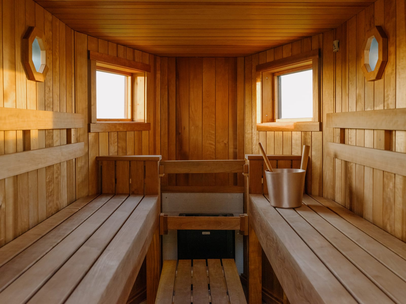 Inside the sauna: twin cedar benches, octagonal porthole windows, bucket and ladle