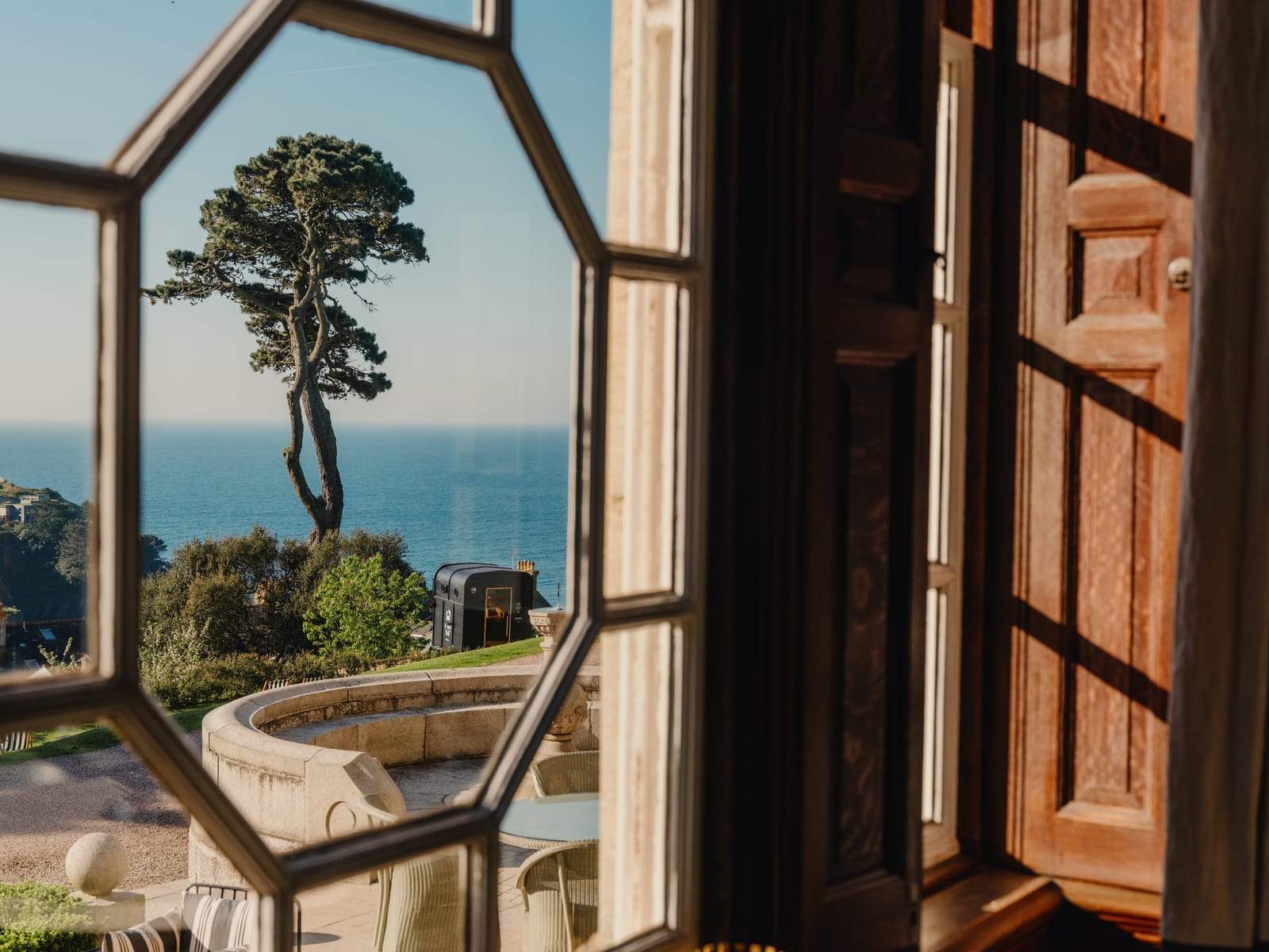 The horsebox sauna and lone pine seen through the leaded window of Fowey Hall Hotel