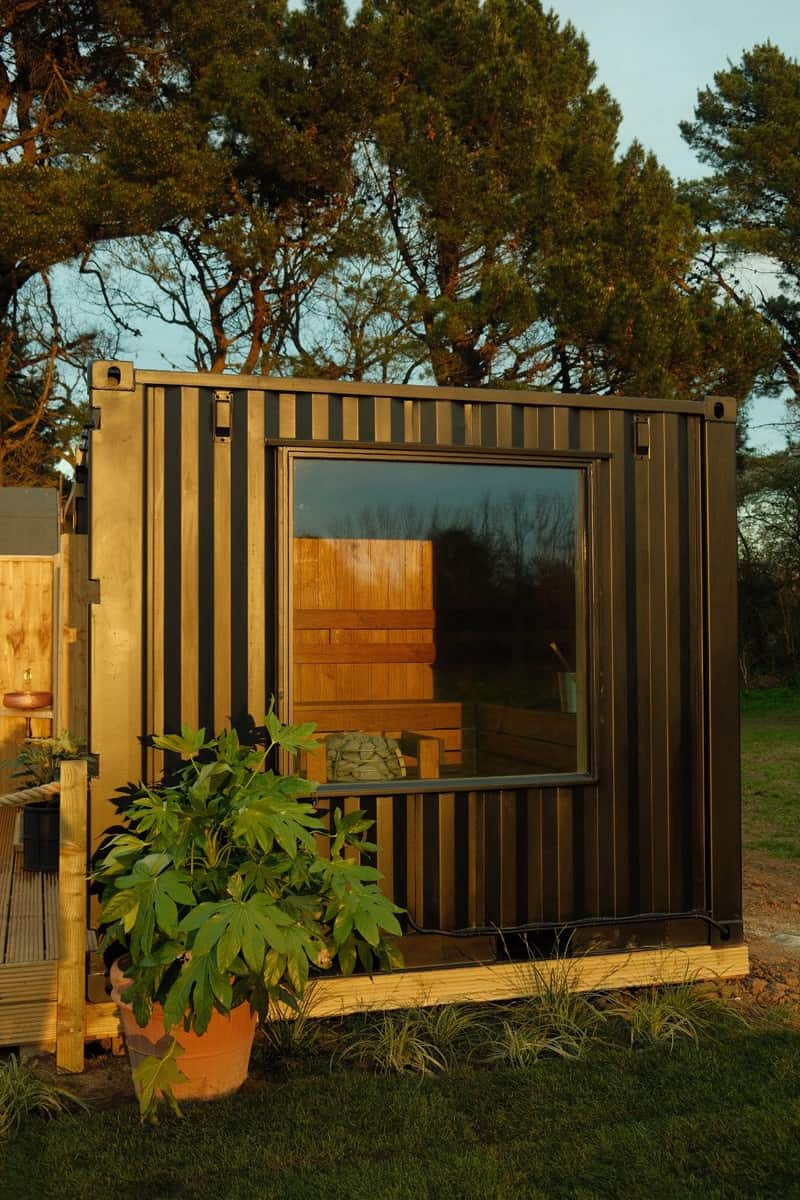 Hidden Sauna Club's black 10ft container sauna with a full-height picture window, in a Norfolk field at golden hour