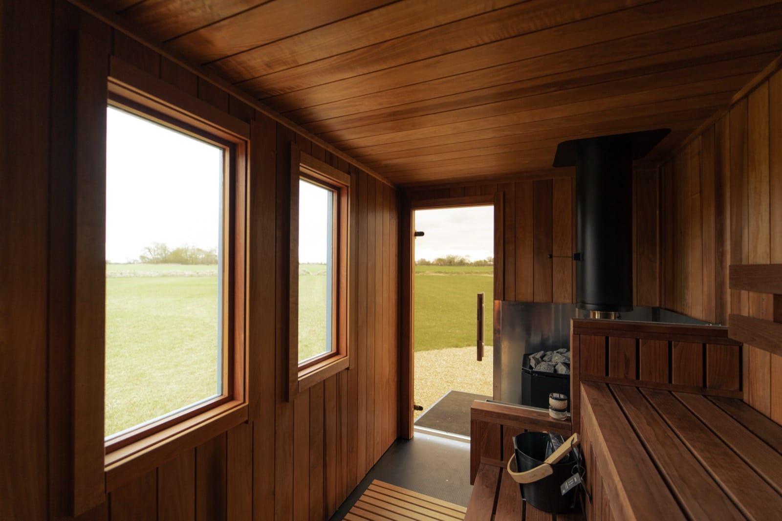 Close-up of the wood-fired stove and stones inside Island Sauna Shack, with the cedar benches beyond