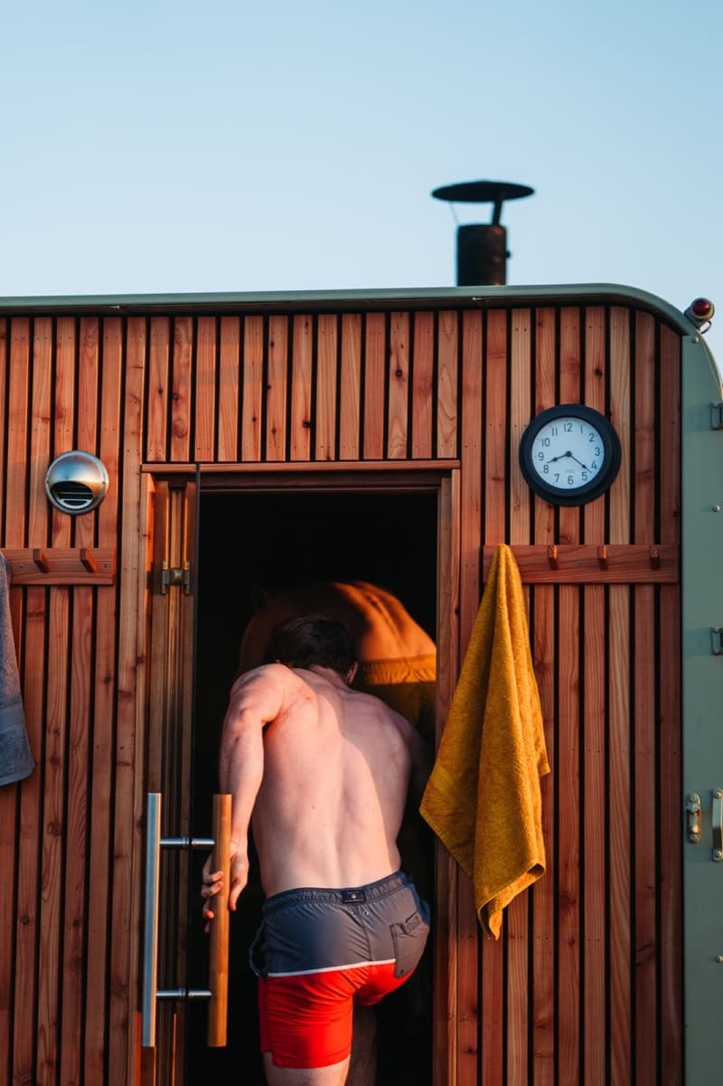 A guest stepping into the cedar-clad horsebox sauna at Vicky's Sauna in the Wild, with the flue and a towel hung on the exterior wall