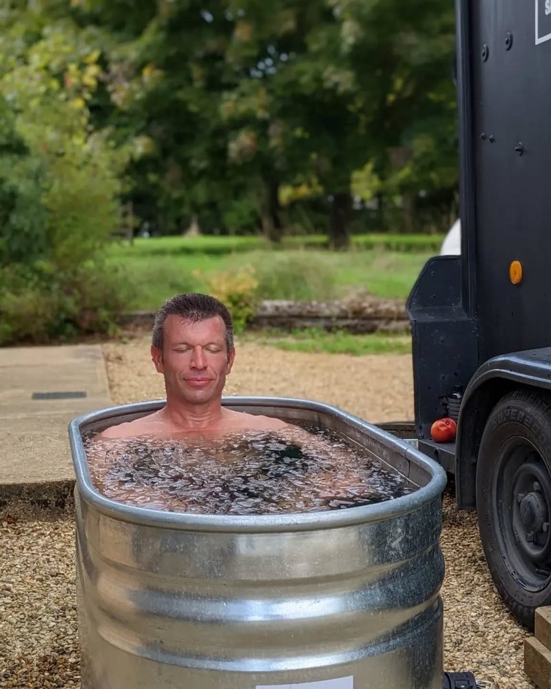 A man sitting calmly in an ice tub beside a black horsebox sauna