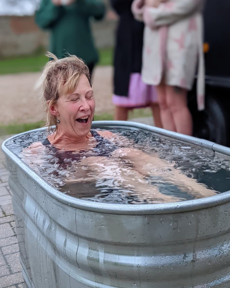 An older woman laughing as she sits down in an ice bath