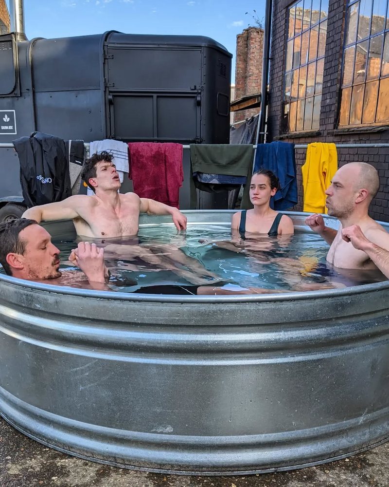 Five people of different ages sharing a big ice tub beside a black horsebox sauna
