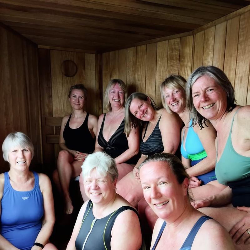 Eight women of different ages smiling together on the benches inside a Sauna Box sauna