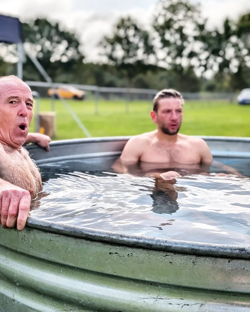 An older man pulling a face at the cold and a younger man, side by side in a round plunge tub
