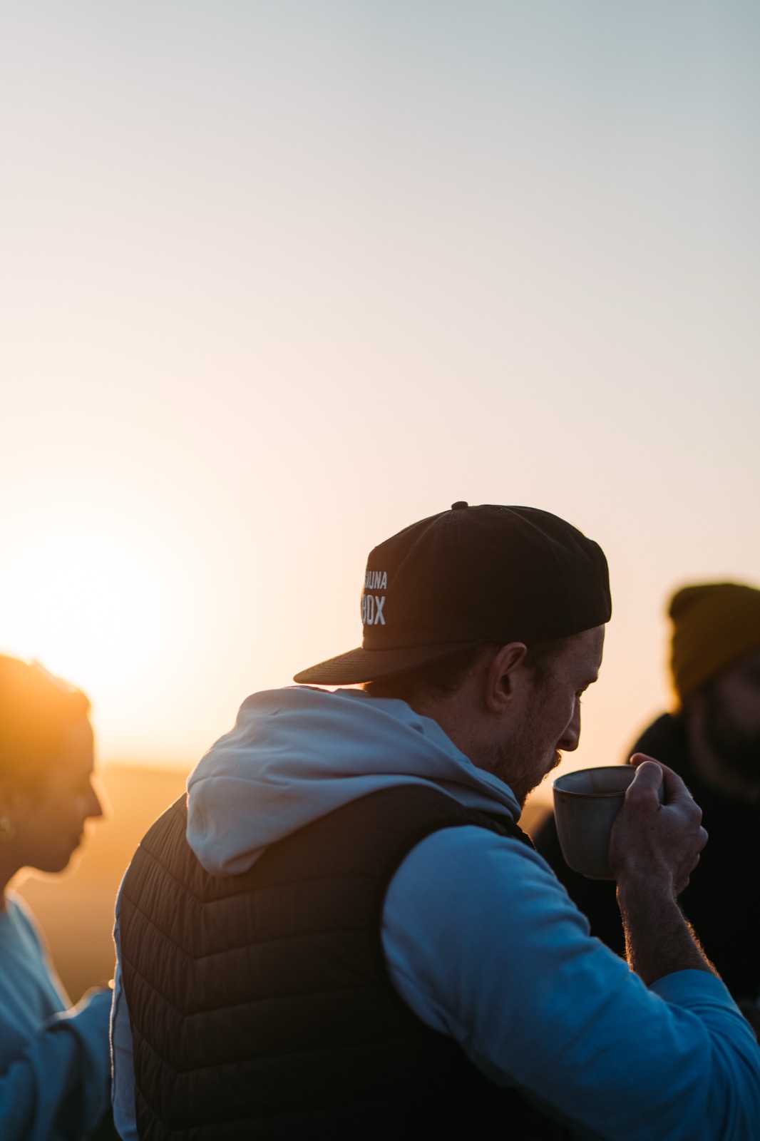 An operator in a backwards cap sips coffee at sunrise outside his sauna