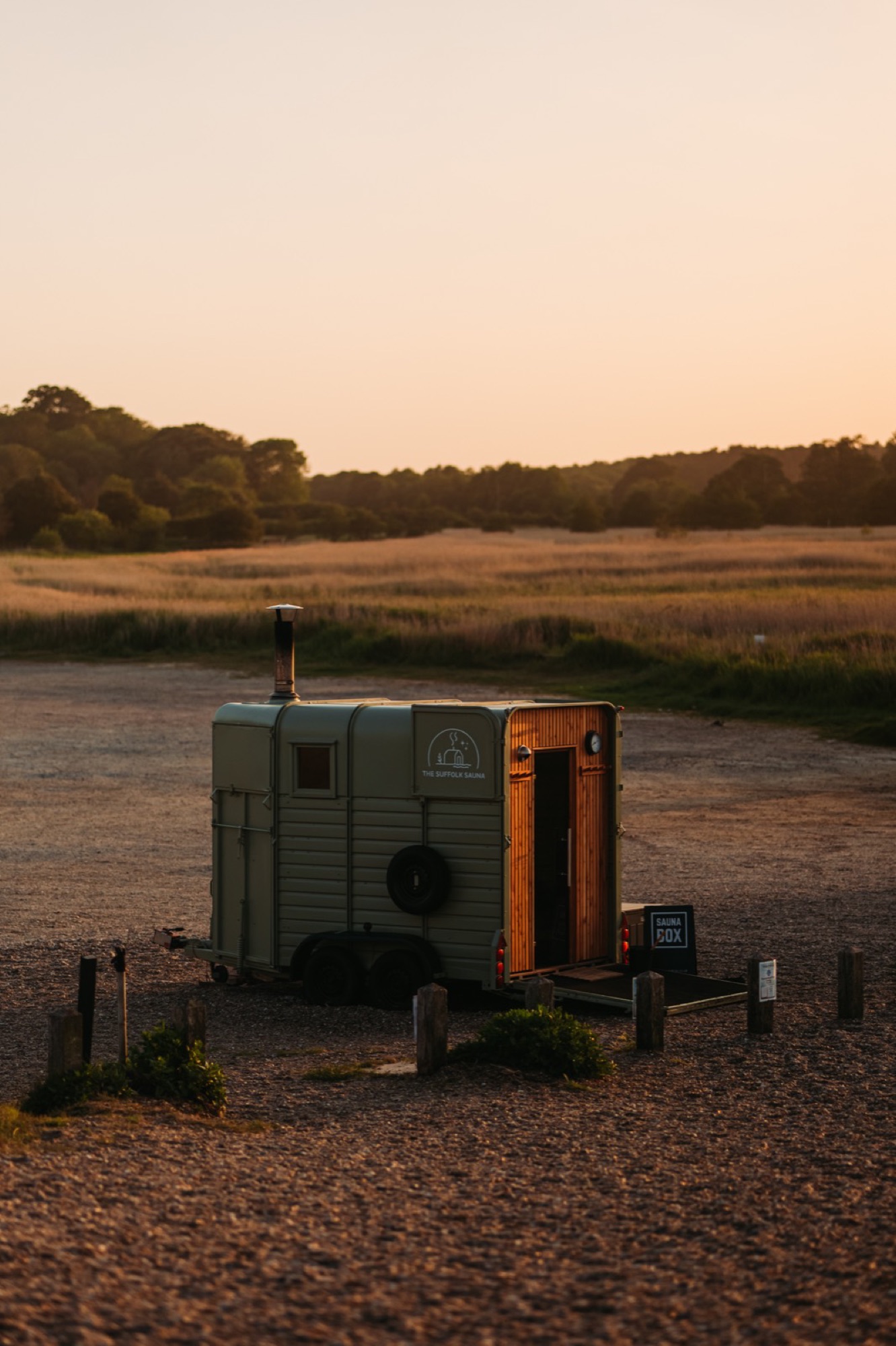 A horsebox-converted wood-fired sauna glowing warm at dusk