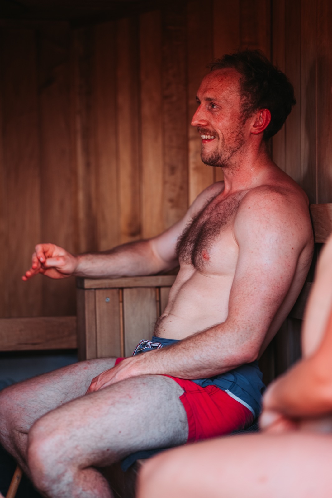 A bather mid-laugh on the warm wooden bench inside the sauna