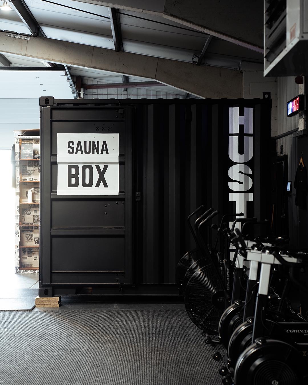 A closed Sauna Box container sauna installed inside a gym, branded door detail