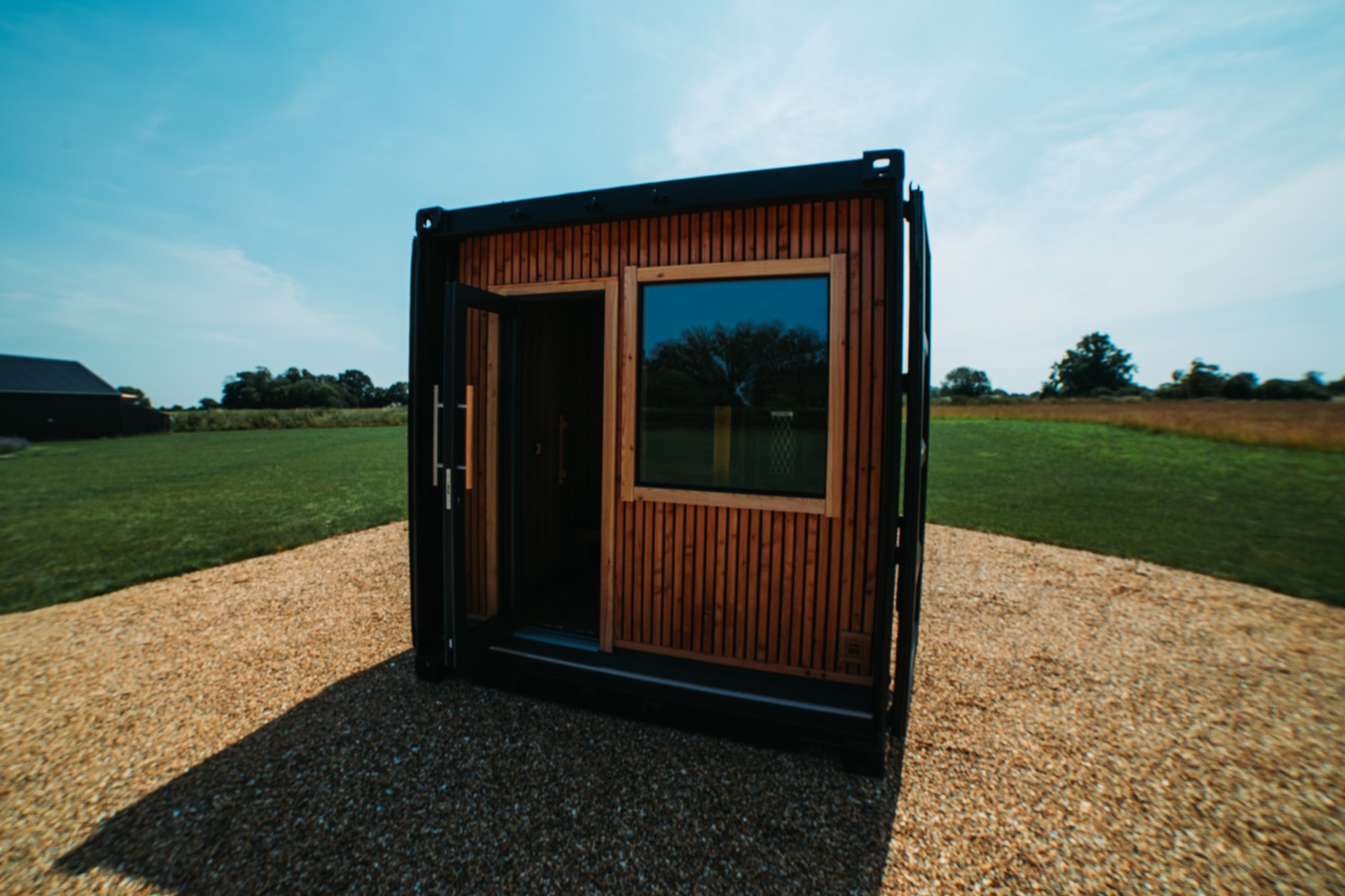 Black Sauna Box container sauna installed in a field with its double doors open