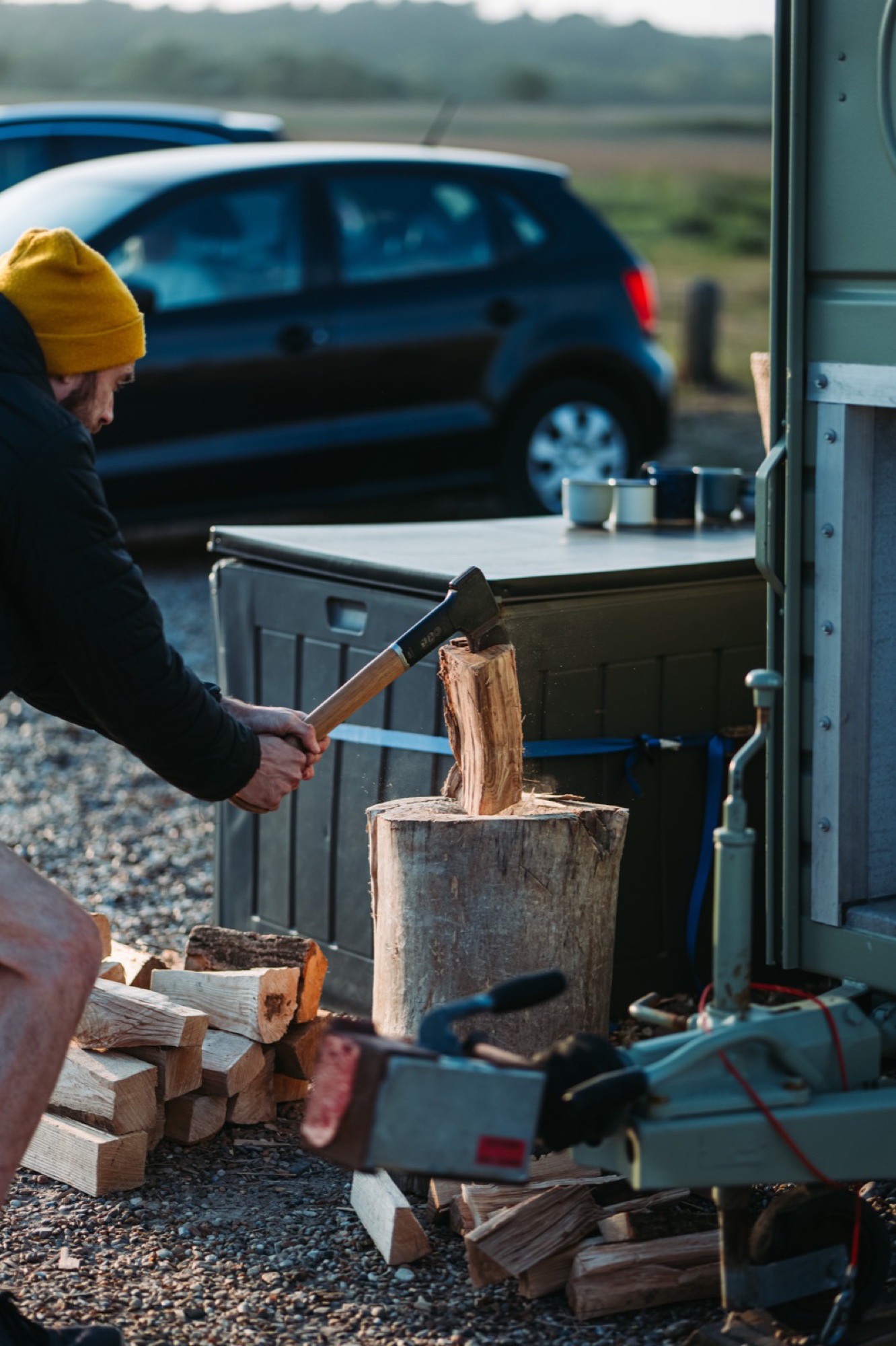 An operator splits firewood beside the sauna in golden evening light, part of the daily work of running it